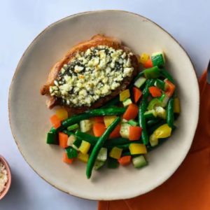 Chimichurri Feta Pork Chop with roasted green beans, peppers, and zucchini on a beige plate